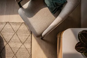 A modern minimalist living room featuring a patterned fabric chair with dark wooden legs, a green cushion, and a woven diamon