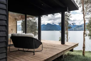 Modern residential deck featuring a wooden platform with a black wicker lounge chair overlooking a serene lake and mountains.
