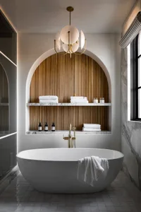 A modern bathroom featuring a large freestanding bathtub surrounded by marble walls and a wooden accent wall with a chandelie