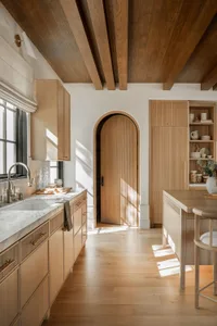 A minimalist kitchen with wooden cabinets and marble countertops, featuring a large island and natural lighting.