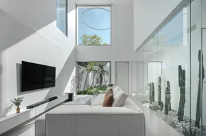 A minimalist living room features a white sofa, modern design, large windows, and a glass wall.
