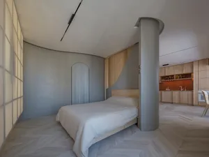 A modern bedroom with light wooden flooring and a bed with a white cover.