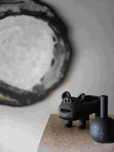 A black ceramic sculpture with a bear-like face and wheels on its back, placed on a textured surface.