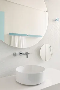 Minimalist bathroom featuring a white ceramic sink with a round shape and a large mirror above it.