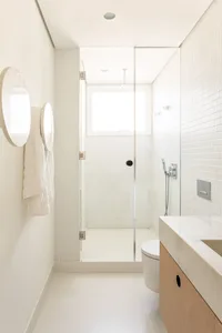 A minimalist bathroom with white tiled walls, a glass shower enclosure, and a sleek floating vanity with a marble countertop.