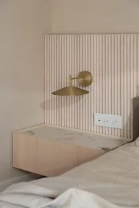 Modern bedroom featuring minimalist design with brass wall lamp, marble surface, and wooden paneling.