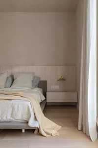 A minimalist bedroom featuring a floating nightstand, wooden headboard, and a window with curtains.