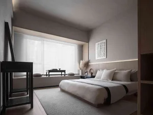 A minimalist bedroom with neutral tones, featuring a bed, nightstand, and artwork above the bed.