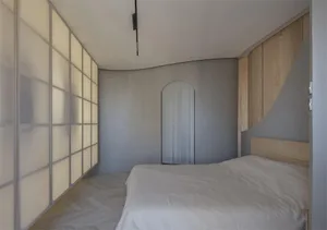 Modern minimalist bedroom featuring a large bed with white bedding, white wood walls, and a large window with frosted glass p