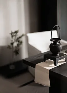 A minimalist room featuring a black vase and a white cushion on a black surface.