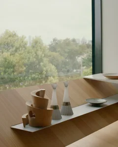 A minimalist table setting featuring wooden and ceramic elements against a large window.