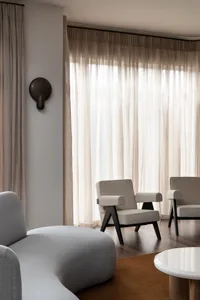 A minimalist living room featuring fabric curtains, a gray sofa, and two modern armchairs with black legs.