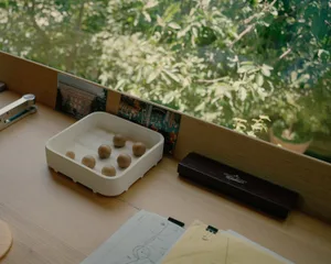 Minimalist office supplies including a container of wooden balls, a stapler, and a box of Georg Jensen pens on a wooden desk.