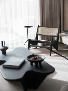 A modern living room featuring a black coffee table with sculptural legs and a black modern lounge chair with bamboo backrest