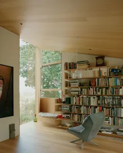 A cozy, modern home library with wooden shelves filled with books, a cozy window seat, and a comfortable armchair.