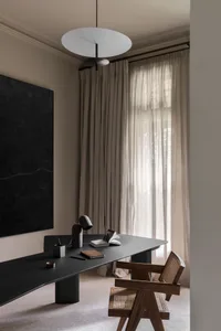 A modern home office featuring a long black desk, a wooden chair, and a linen curtain by the window.