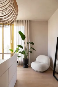 A modern living space with light-colored flooring, minimalist furnishings, and a large window with sheer curtains.