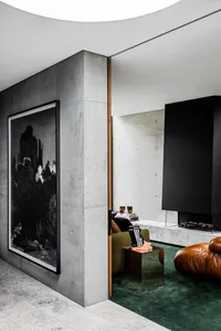 A modern living room featuring a concrete wall with a large black and white photographic print, a green carpet, and a brown l