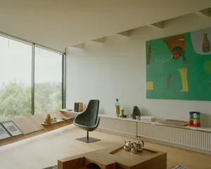 A modern living room with a wooden floor, a black chair, and a green abstract painting on the wall.