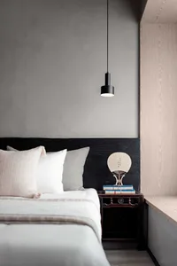A modern minimalist bedroom with a bed, pillows, and a small side table with books and a decorative item.
