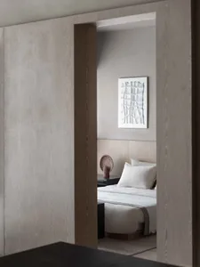 A minimalist bedroom with a wooden headboard and grey walls, featuring a white bedspread and decorative vase on the nightstan