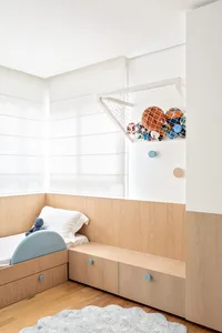 A modern minimalist children's bedroom featuring a bed with a blue headboard, built-in storage units, and a net holding sport