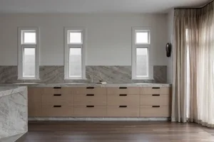 Modern minimalist kitchen with natural wood cabinets and marble countertop.