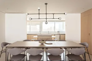 A modern minimalist kitchen space featuring a wooden dining table, concrete kitchen island, and glass pendant lights.