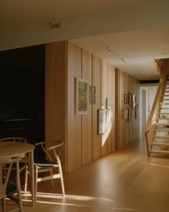 A modern residential corridor with wood paneling, framed art, and a staircase.