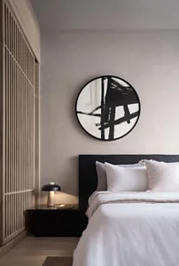 A minimalist bedroom with a black-framed bed, white bedding, neutral-toned wall paint, and a black side table lamp.