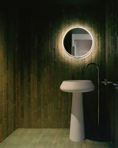 A minimalist bathroom with a green-tiled wall and white freestanding sink.