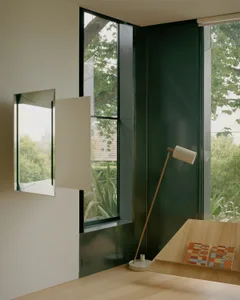 A minimalist office space featuring wooden desk, glass window, and metallic lamp.