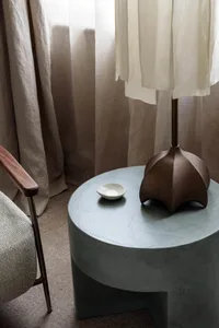 A modern concrete side table with a bronze lamp on it.