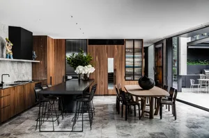Modern kitchen dining room featuring wooden and concrete finishes with a long black table and white bar stools.