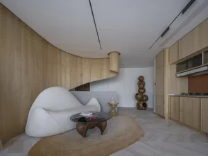 A modern living room featuring a curved, minimalist sofa and a unique circular coffee table with a wood grain base and glass 
