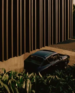 Black vintage car parked next to a modern metal building, surrounded by greenery.