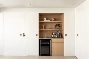 A modern, minimalist home bar area with wooden shelves, a mini fridge, and bottles of alcohol.