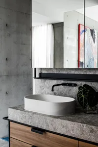 A modern bathroom with a white countertop and sink, featuring a black faucet and a plant in a glass vase.