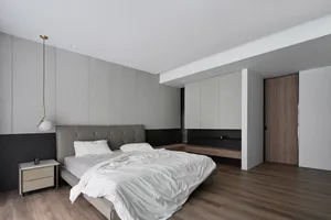 A minimalist bedroom featuring a bed with a textured headboard, white bedding, and a wooden floor.