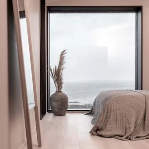 Minimalist bedroom with a wooden floor, a fabric-covered bed, and a decorative vase