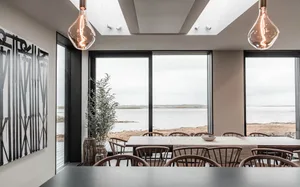 Modern dining room with wooden furniture, glass windows and metal light fixtures.