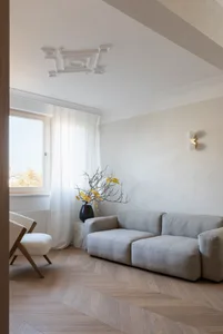 Modern minimalist living room with a light grey sofa, white armchair, and a marble side table with a plant.