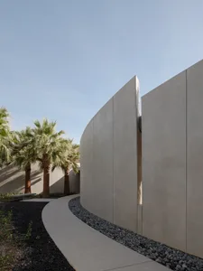 Modern, sleek, concrete exterior of a building with curved walls and palm trees in the background.