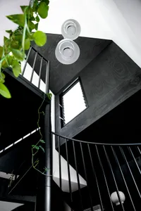 A modern interior staircase with black metallic railings and railings, featuring green vines climbing the sides.