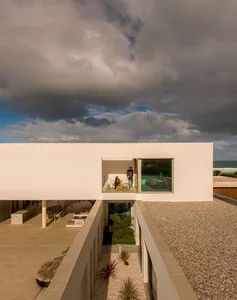 A modern, minimalist house with a white exterior, concrete walkways, and large glass windows.