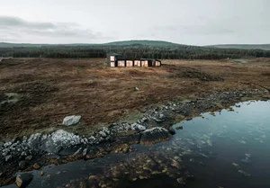 A modern exterior lodge with black steel and glass features, situated in a remote natural landscape.