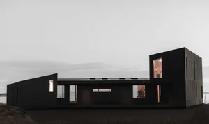 A modern house exterior with a minimalist design and black painted walls, featuring large windows and a simple geometric shap