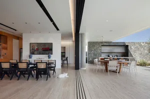 A modern living and dining room with concrete walls, minimalist furniture, and a large window for natural light.
