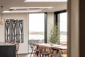 Modern minimalist dining room featuring wooden furniture and large windows overlooking a scenic view.