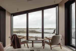 A minimalist living room with a glass wall, wooden furniture, and carpet